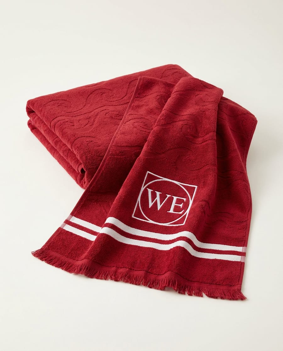 Red jacquard beach towel with white border stripes and a WE monogram